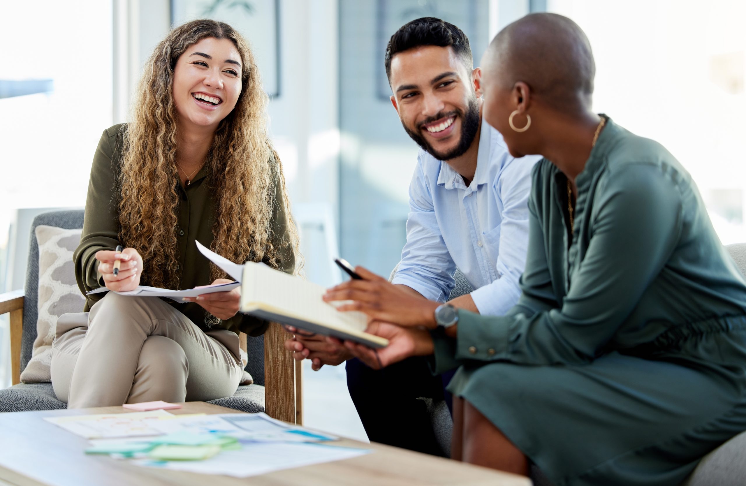 Three colleagues smiling and collaborating during a casual office meeting.