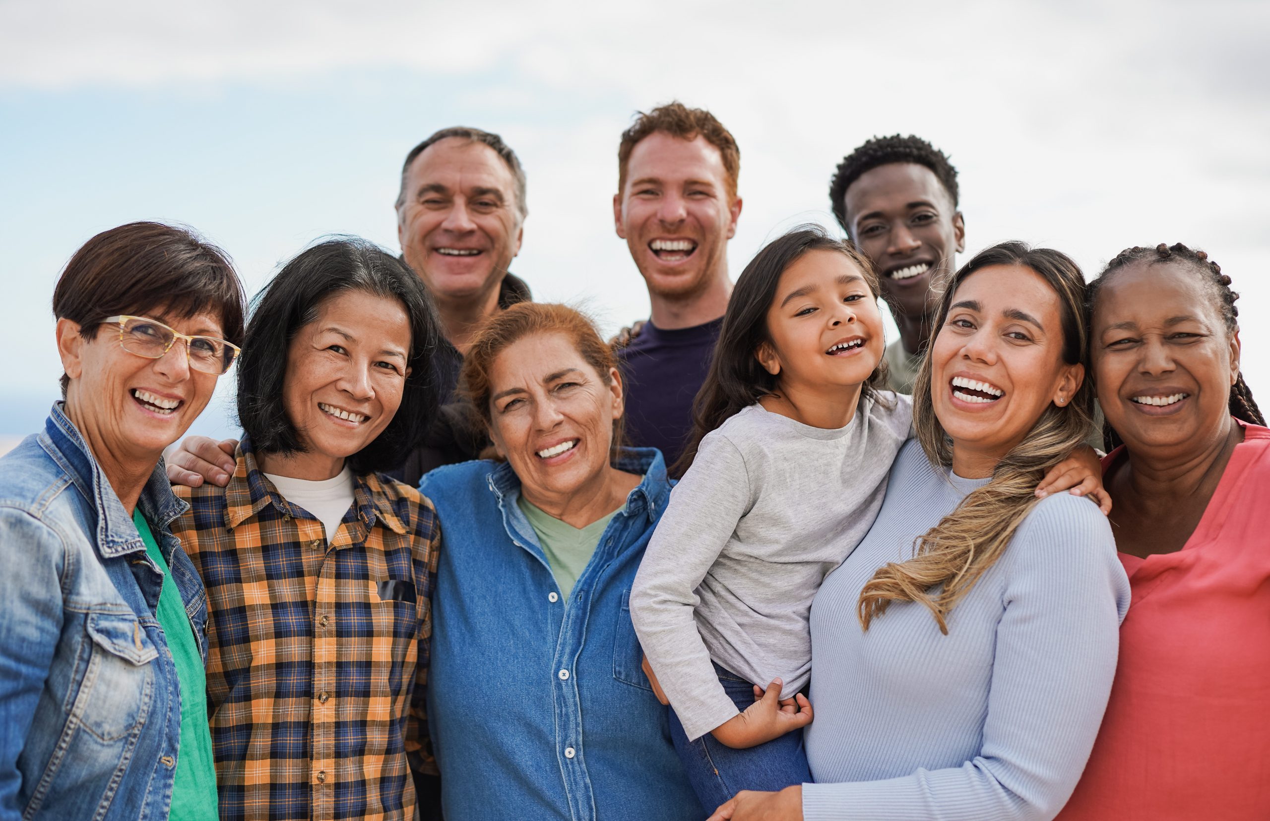 A diverse multigenerational group of people smiling together outdoors.