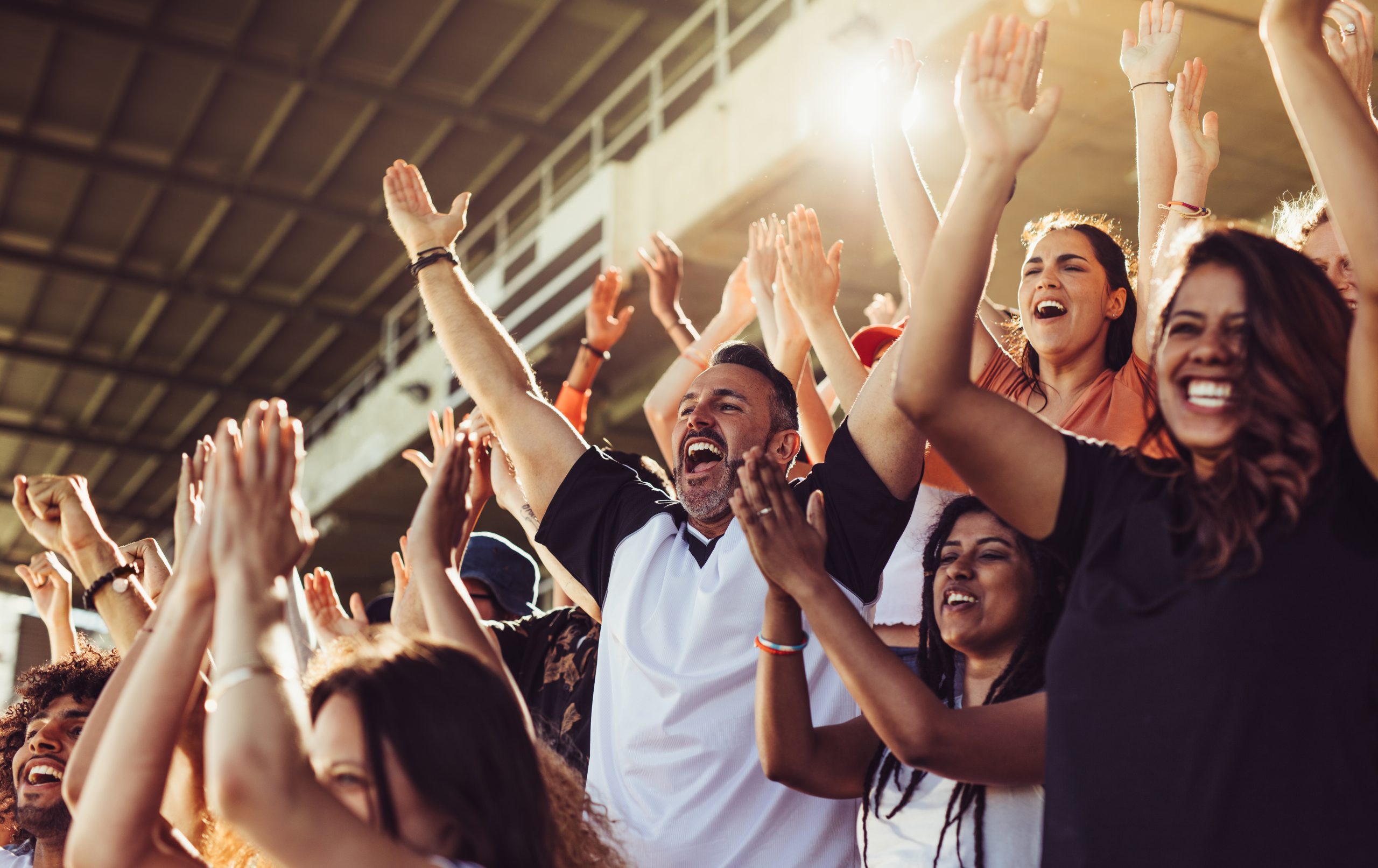 A crowd of enthusiastic fans cheering with hands raised in a stadium